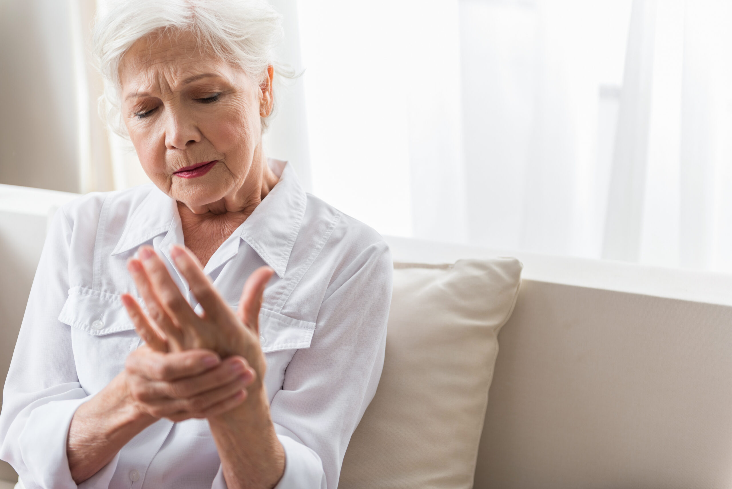 Arm ache. Gray-haired mature woman is suffering from arthritis. She is looking at her hand and feeling awful pain. Copy space in the right side